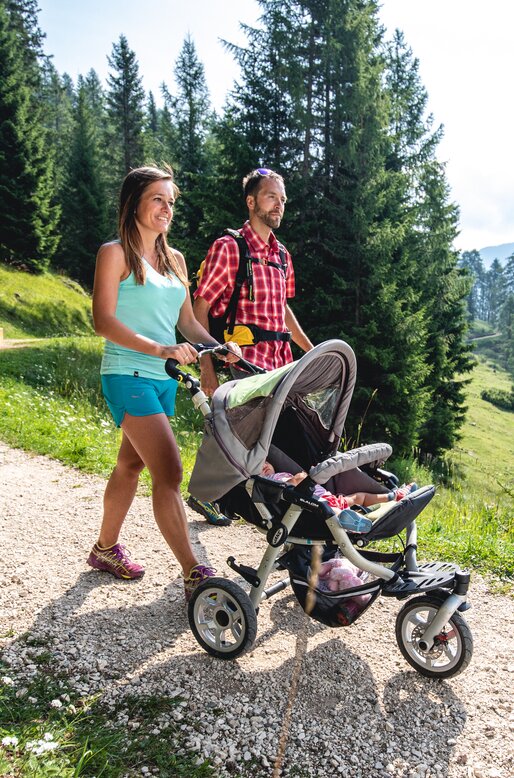 Genitori con passeggino camminano su strada sterrata a Latemar Dolomites | © APT Fiemme e Cembra - Alice Russolo