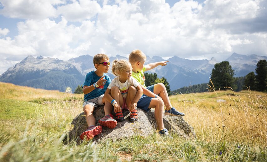 Tre bambini seduti su una roccia osservano il paesaggio | © APT Fiemme e Cembra - Gaia Panozzo