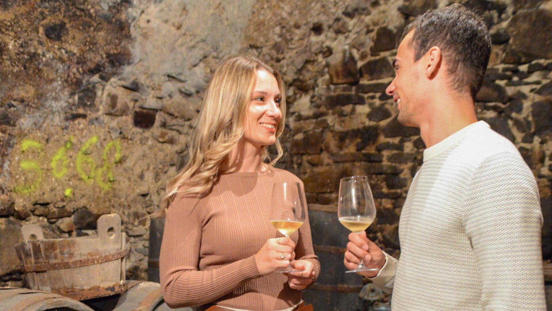 Coppia assaggia del vino bianco tra le piccole botti di una cantina  | © APT Fiemme e Cembra