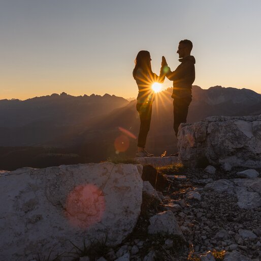 Coppia all'alba in montagna; i raggi del sole passano tra le loro mani giunte | © APT Fiemme e Cembra - foto di Gaia Panozzo