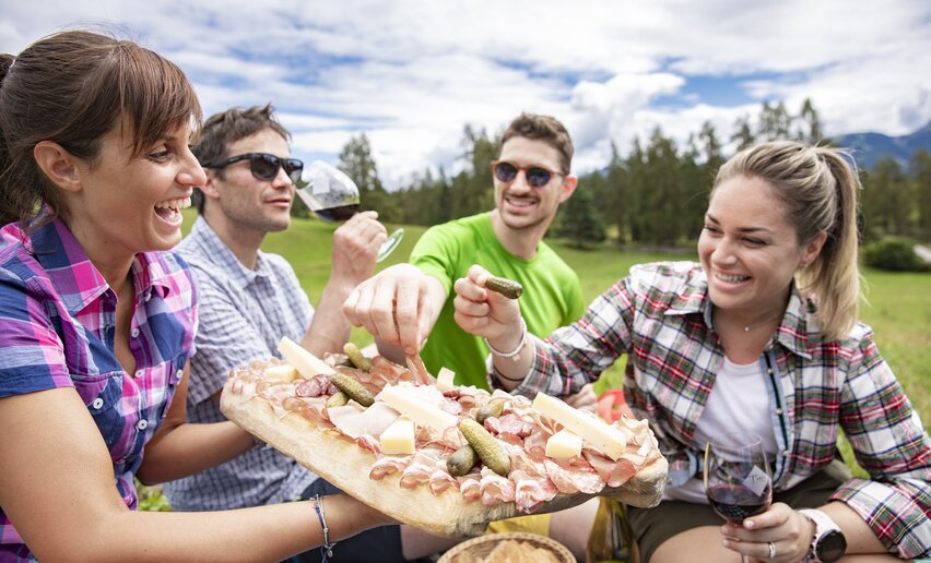 Quattro amici condividono un tagliere di salumi e formaggi in località Ganzaie | © APT Fiemme e Cembra - Federico Modica