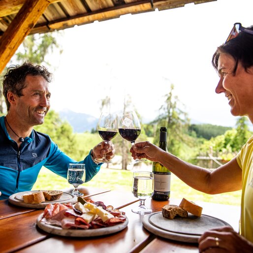 Coppia fa aperitivo in un tavolo all'aperto con tagliere misto e vino rosso | © 	 APT Fiemme e Cembra