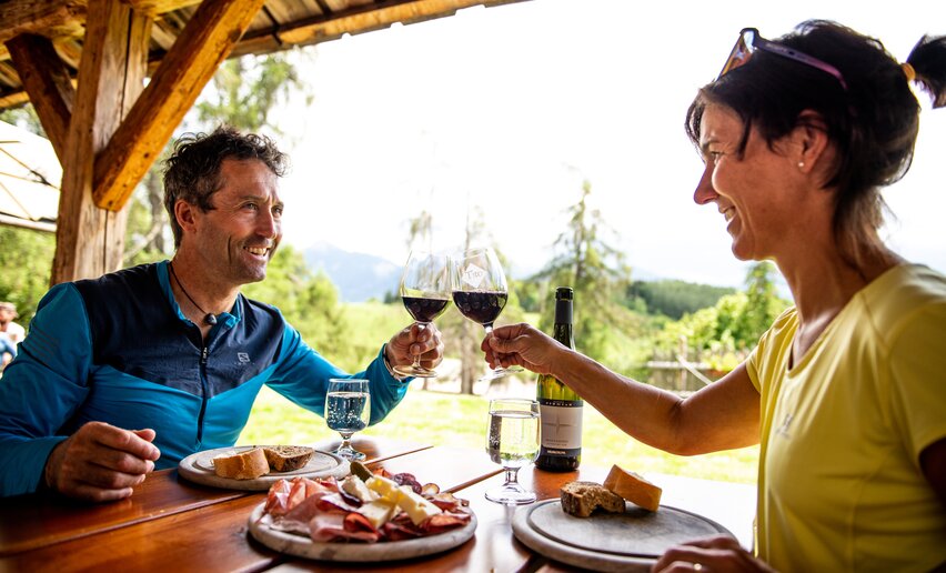 Coppia fa aperitivo in un tavolo all'aperto con tagliere misto e vino rosso | © 	 APT Fiemme e Cembra